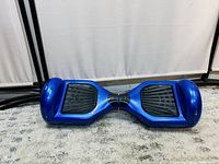 Full view of blue hoverboard scooter on carpeted floor, showing both wheels and foot pads.