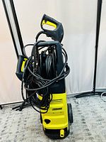 Front and side views of Karcher pressure washer showing the high-pressure hose coiled around the body, the spray gun handle, and power cord.