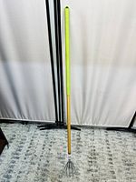 Front view of the gardening tool showing wooden handle with green grip and metal claw head.