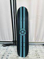 Photo of the skateboard deck showing black grip tape with two vertical blue stripes and center logo.