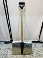 Full view of snow shovel showing wooden handle with black D-grip and a large metal blade in good condition.