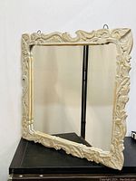 Frontal view of square mirror with intricately carved off-white frame showing unique organic vine and leaf design.