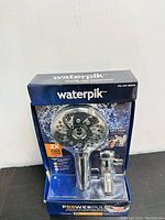 Front view of Waterpik PowerPulse shower head in packaging showing 8 spray settings and water pause feature.