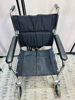 Front view of a black-seat foldable wheelchair with metal frame and armrests.