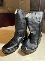 Pair of black leather cowboy boots displayed upright on table, showing both boots side by side.