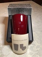 Red lacquered drinking glass in silver textured box with foam insert and label 'Shibuichi: Urushi Glass'.