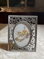 Front view of metal frame showing floral and vine pattern with oval image depicting chalice, wheat, grapes, and Bible for First Communion.