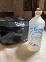 Photo shows black GemOro 26QTH ultrasonic cleaner next to bottle of Gesswein multi-purpose ultrasonic cleaning solution on a table.