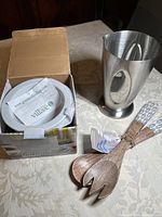 View of dip chiller in box, stainless steel measuring cup, and wooden salad servers on table