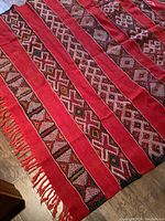 Full view showing the alternating red stripes and patterned bands with fringe on one end.