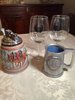Photo shows two large clear wine glasses with Kentucky Wineries Association logos, one decorative Gerz German beer stein with a pewter lid featuring a horse-drawn carriage scene, and one pewter beer mug with embossed Delaware state seal.