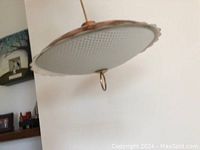 Underside view of white pressed glass dome shade with raised dot pattern and scalloped edge suspended from copper hardware
