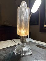 Pressed glass table lamp turned on showing detailed geometric and herringbone pattern on shade and ribbed pattern on base.