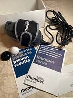 Massager unit with adjustable strap, black and white massage spheres, electrical cord, and manuals laid out on table.