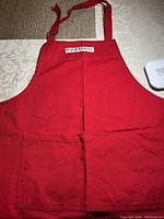 Full view of the red apron with front pocket and logo, lying flat