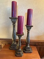 Three antique brass candle holders of different sizes each holding a red pillar candle.