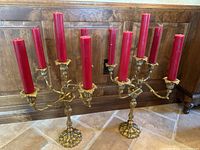 Pair of brass candelabras displayed side by side, each holding four tall red pillar candles, showing full height and width.