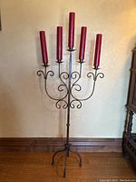 Full view of the tall metal candelabra with five red candles installed, showing the height and base design.