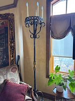 Full view of candle lamp standing next to an upholstered chair and window, showing metal construction and candle-shaped bulbs.