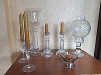Group shot of six clear glass candleholders including three with globe covers and three with taper candles