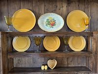 Overall display of all dishes on wooden shelves showing yellow plates, squash platter, yellow goblets, heart dish, and salt and pepper shakers.