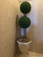 Full view of the artificial topiary tree with two green spherical balls and brown trunk in a decorative indoor space.