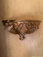 Front view of one gold painted ornate plastic wall shelf mounted on wall