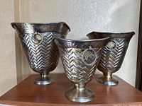 Three hand-pounded metal buckets of varying sizes displayed on a wooden surface, showing overall shape, pattern, and metal finish.