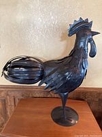 Side view of metal rooster sculpture showing detailed metal feather layering, comb, wattle, and curled tail