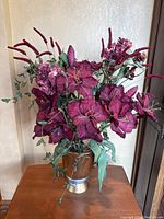 Overall view of the red artificial floral arrangement with various red flowers and green leaves in a gold vase.