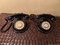 Two black push button rotary dial telephones side by side on brown textured surface