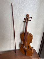 Full view of the wooden violin alongside the bow, showing size and detail against a patterned wall.