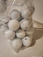 Clear plastic bag containing 50 assorted white golf balls with visible wear and markings.