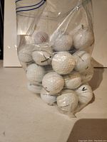 Plastic bag containing 50 assorted, used white golf balls with various brand markings, showing signs of wear and scuffs.