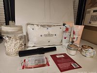 Photo showing luxury bath pillow, two Paradise brand tubes, two scented candles, Q-tip container, mascara, and informational cards.