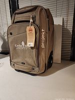 Front view of new brown Projekt carry on luggage with Cedar Brand Golf Club logo and tag attached