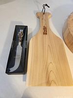 Rectangular wooden cheese board with handle, cheese cutter in black box with decorative handle next to it