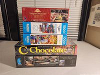 Stack of four puzzle boxes, focusing on 'C is for Chocolate' (bottom) and 'Impressions' (top) showing unopened condition