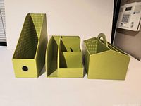 Photo of four green desk organizers arranged on a desk surface showing front and side views.