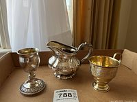 Display of three pieces: footed goblet, cream pitcher, handled cup