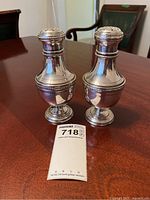 Two silver-plated salt and pepper shakers on wooden table, with lot sticker