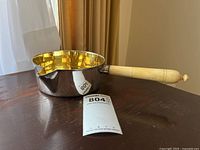 Side view of silver sauce pot with ivory handle and pouring spout on dark wood surface