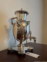 Full front view of urn on stand showing body, handles, spigot and tripod base.