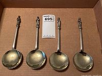 Overview of four spoons in storage box with lot card