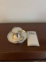 Front view of round silver inkwell on wooden surface