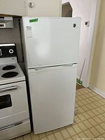 Front view of white GE top freezer refrigerator next to a stove.