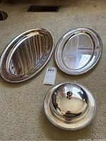 Two oval silver trays and one small covered serving dish arranged on floor, showing condition and relative sizes