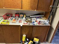 Wood countertop with various small household, electrical and hardware items including light bulbs, organized in small containers.
