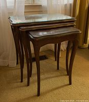 Photo showing the full set of three wooden nesting tables stacked, largest with shaped glass top, medium and small without glass.