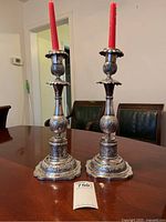 Pair of tall silver and wood candlesticks with red tapers on wooden table